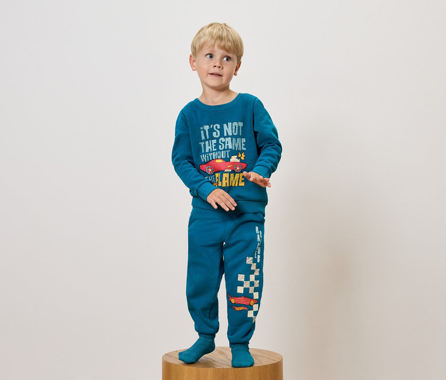 Junge im blauen Pyjama mit Autoaufdruck steht auf einem Holzsockel.