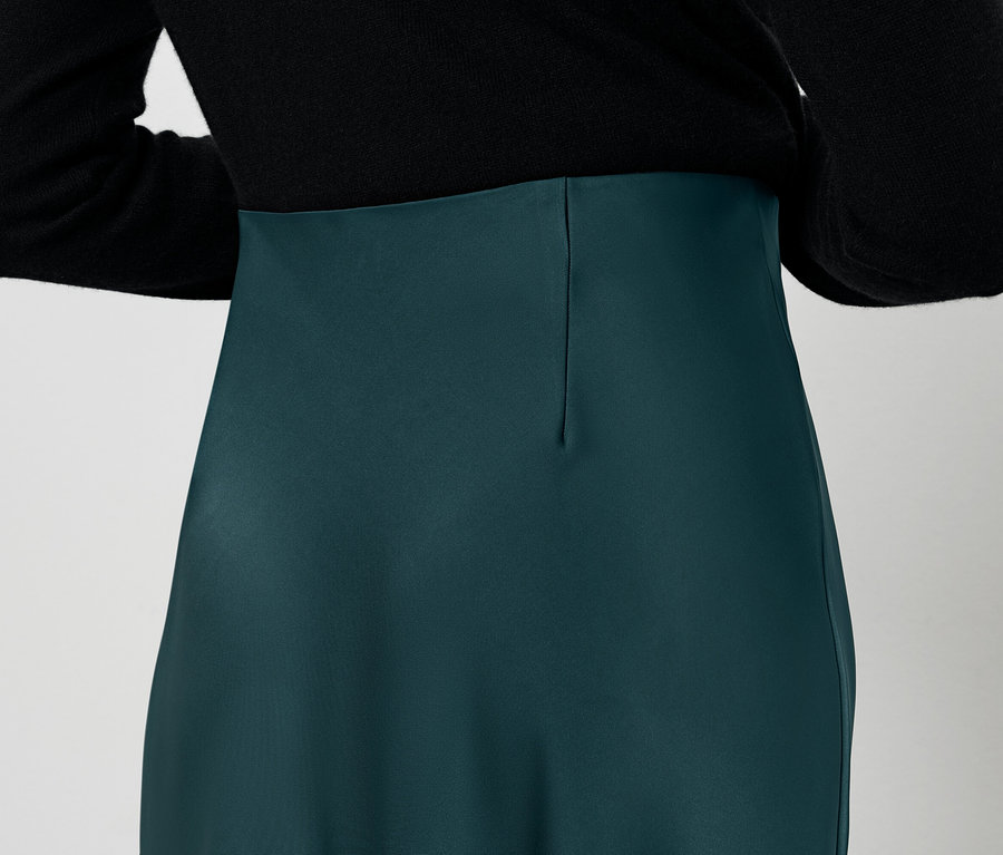 Rückansicht einer Frau mit schwarzer Bluse und grünem Rock.