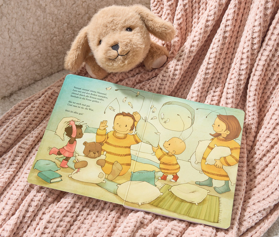 Ein Plüschhund liegt auf dem Buch "Die Baby-Hummel Bommel" und einer rosa Strickdecke.