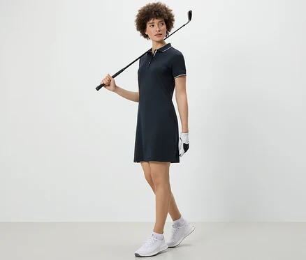 Frau hält Golfschläger über der Schulter und trägt ein Sportkleid.