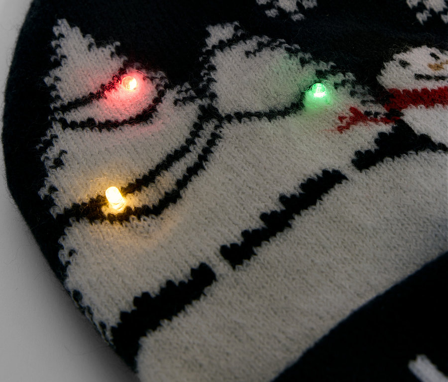 Detailaufnahme einer schwarz-weissen Strickmütze mit Schneeflocken und Schneemännern, verziert mit bunten Lichtern.