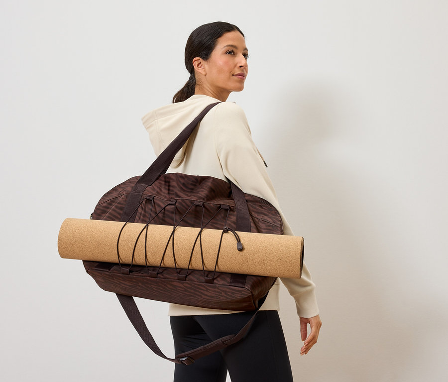 Frau trägt eine braun gemusterte Sporttasche mit einer Yogamatte darüber
