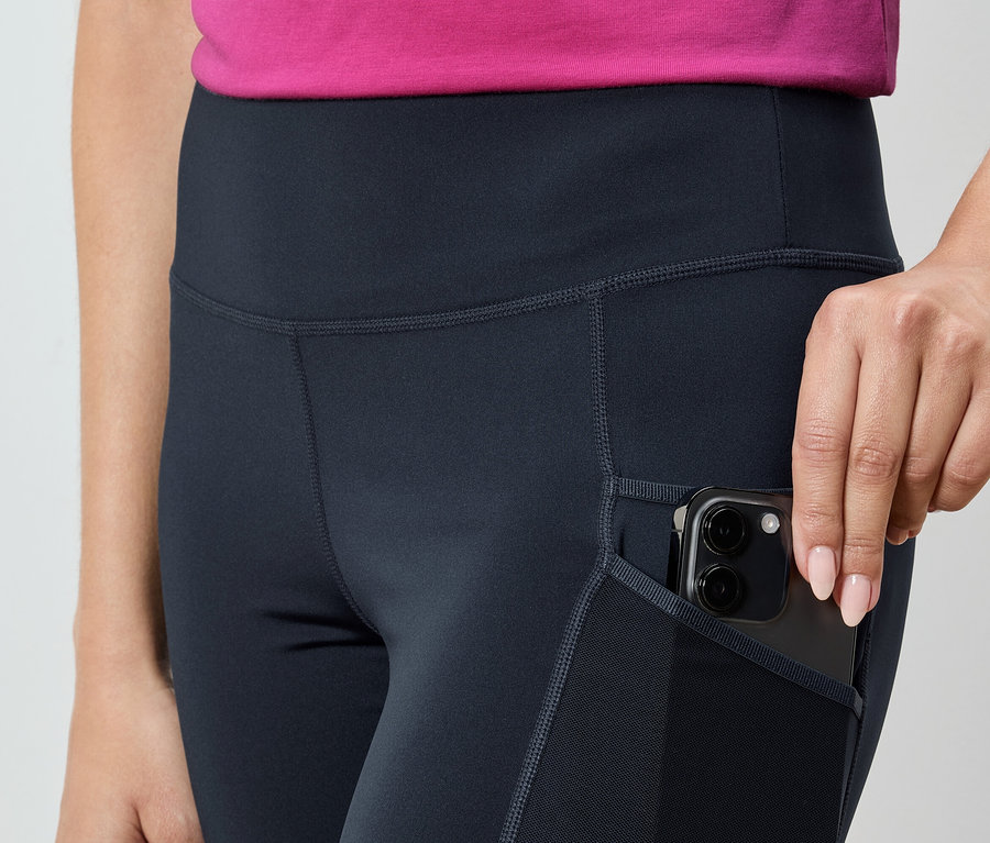 Frau steckt ein Smartphone in die Tasche einer marineblauen Leggings.
