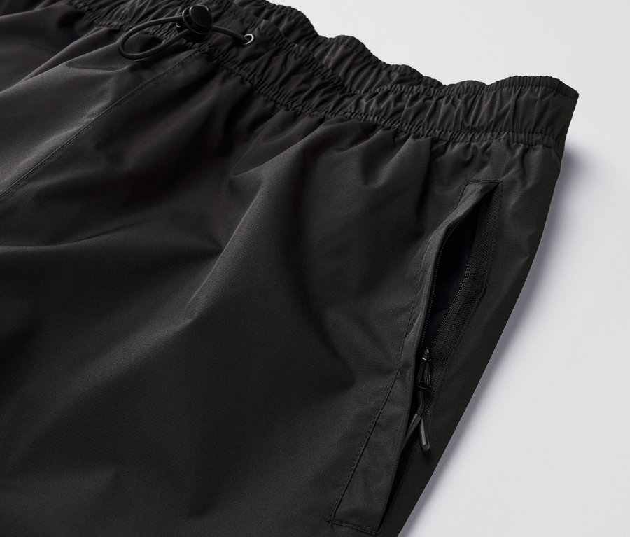 Detailansicht einer schwarzen High-Tech-Regenhose mit elastischem Bund und Reissverschlusstasche.