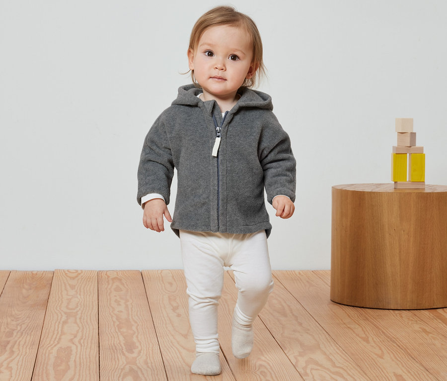 Kleinkind geht in grauer Baby-Fleecejacke und weißen Leggings.