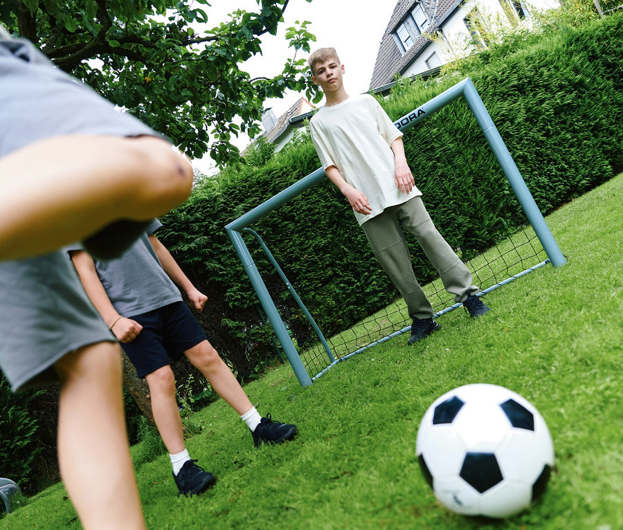 Eine Gruppe Kinder spielt Fußball auf einer Wiese mit einem HUDORA Fußballtor »Expert 300«.