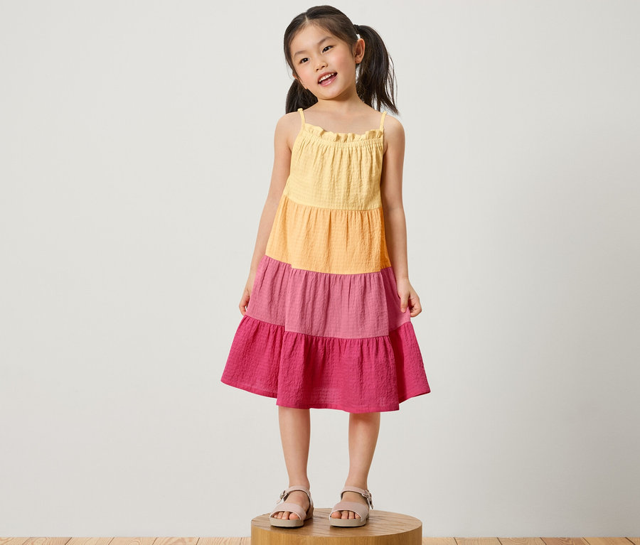 Mädchen steht auf einem Holzsockel und trägt ein Kinder-Webkleid.