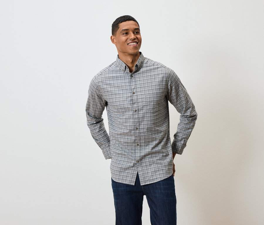 Lächelnder Mann posiert in einem grau karierten Langarmhemd und dunkelblauen Jeans.
