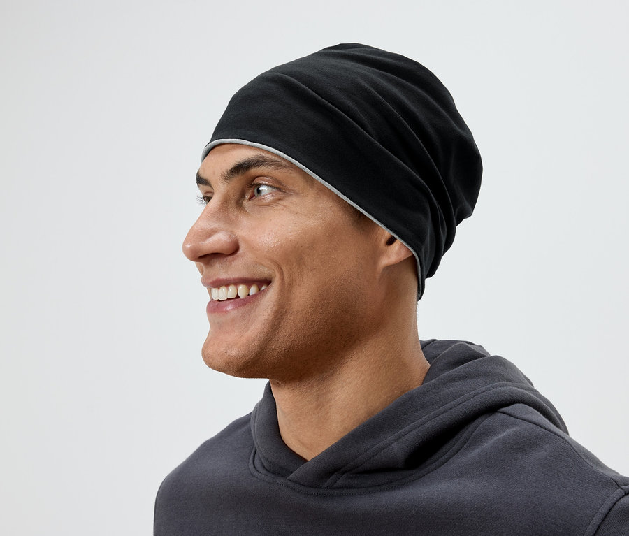 Profilansicht eines lächelnden Mannes mit einer schwarzen Mütze und einem grauen Hoodie.