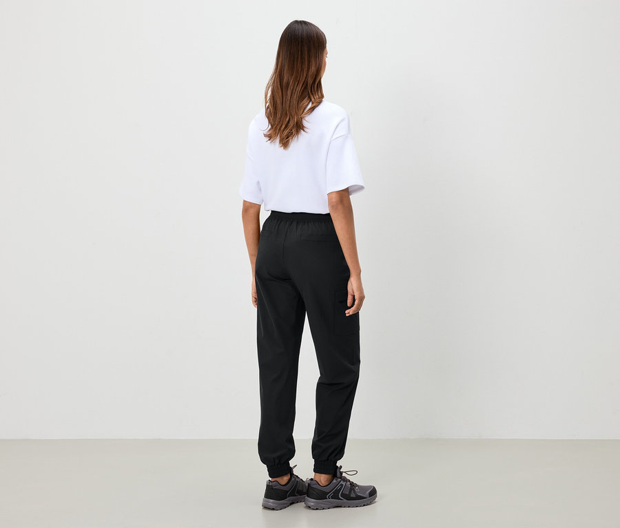 Frau steht mit dem Rücken zur Kamera und trägt ein weißes T-Shirt, schwarze Hosen und graue Schuhe.