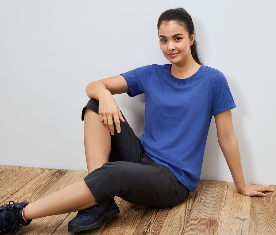 Frau sitzt auf dem Boden und trägt ein blaues Sportshirt.