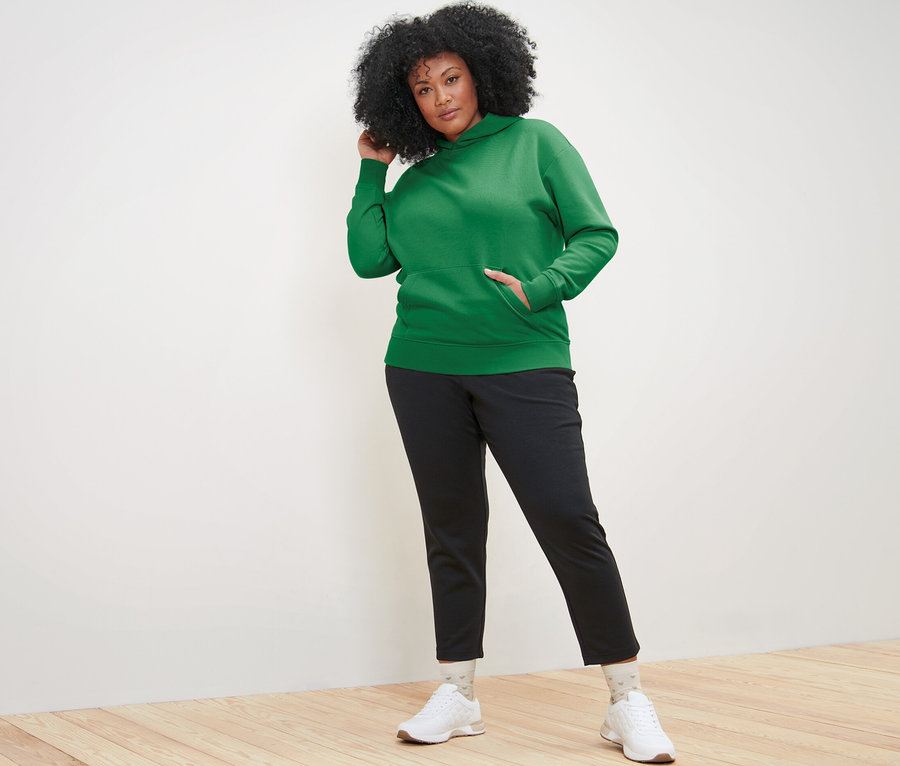 Frau posiert in grünem Hoodie und schwarzer Hose.