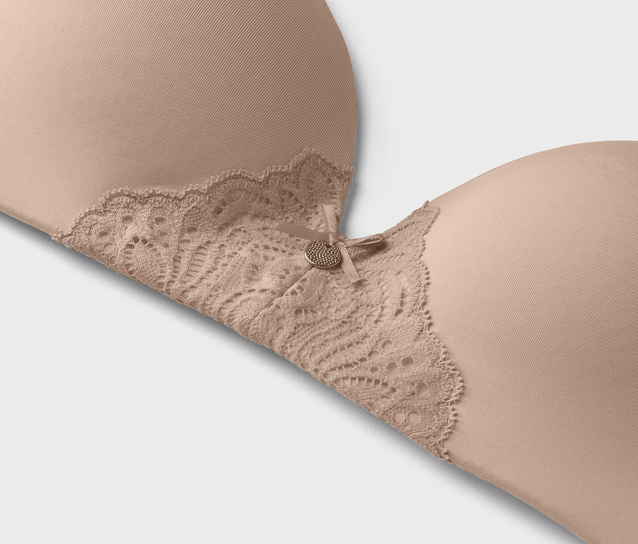 Nahaufnahme eines hautfarbenen BHs mit Spitzenbesatz und kleinem Zierknopf.