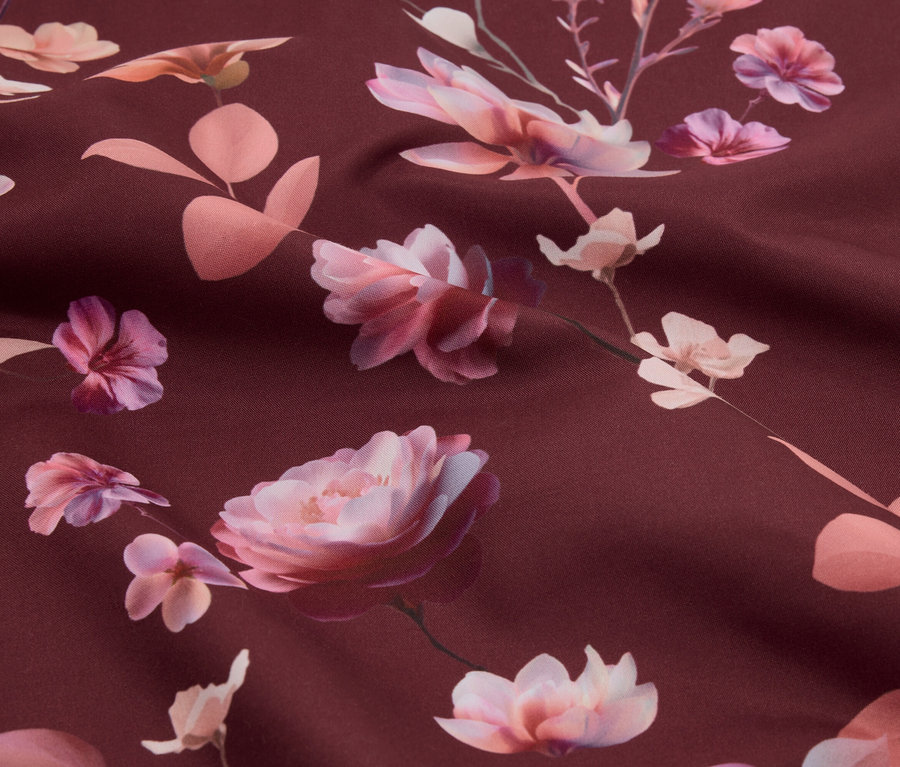 Nahaufnahme eines Stoffes mit einem Muster aus rosa Rosen und Blättern auf einem weinroten Hintergrund.