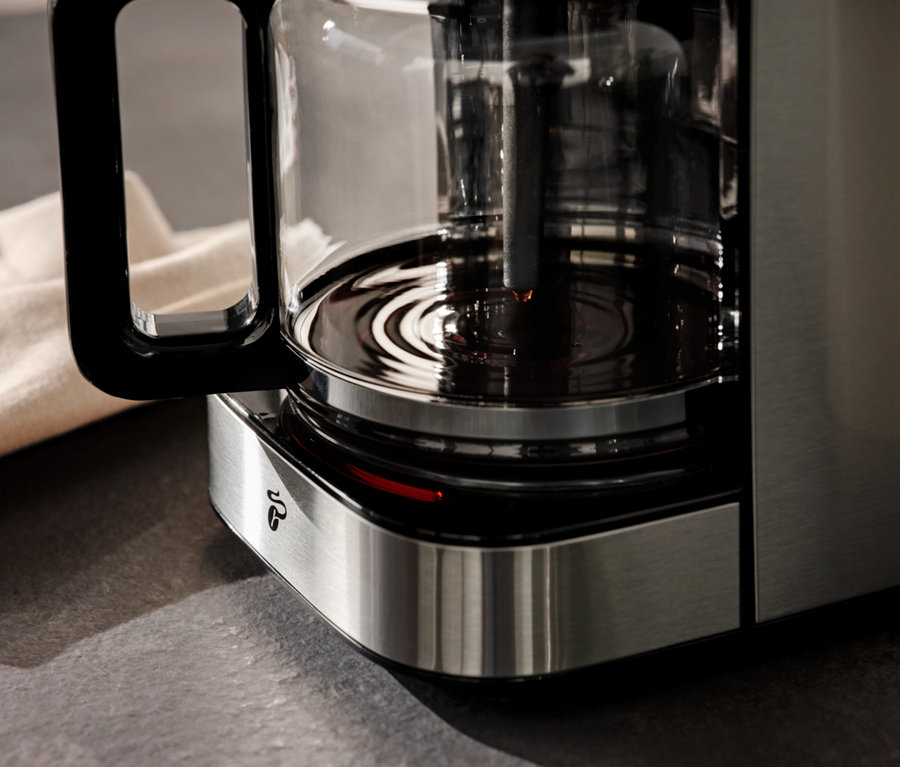 Detailansicht einer Kaffeemaschine mit Kaffeekanne und einem beigen Tuch im Hintergrund.