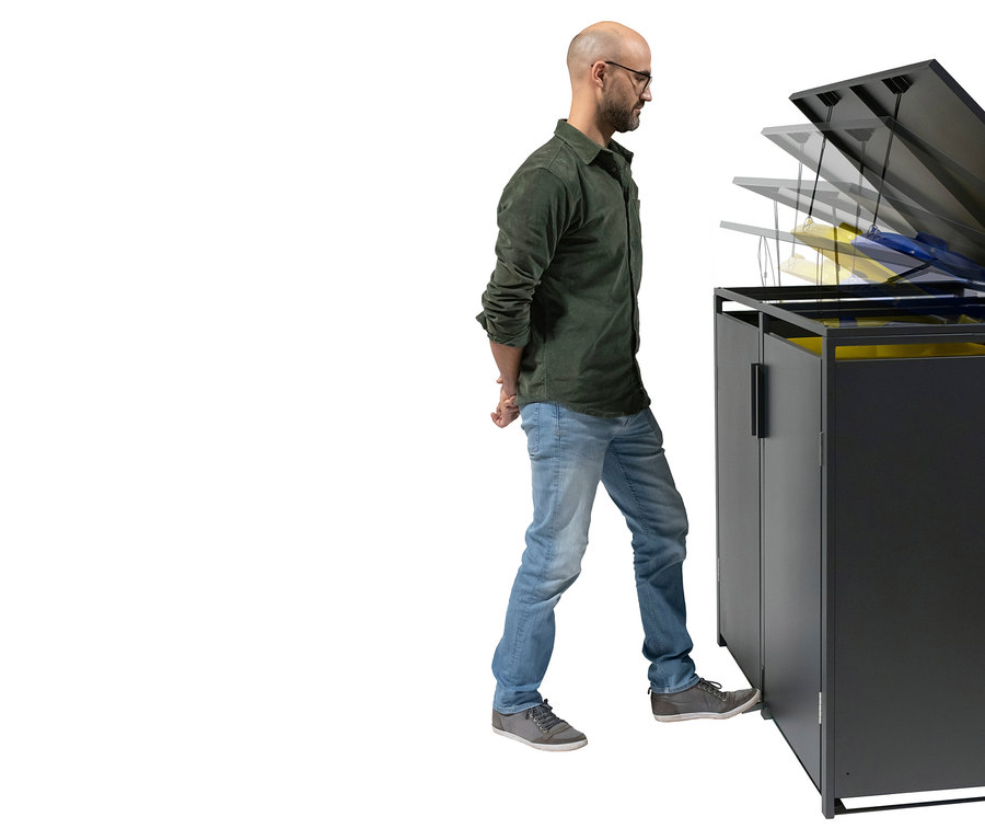 Ein Mann mit Brille öffnet einen schwarzen Müllschrank mit dem Fuß. Im Inneren befinden sich gelbe und blaue Müllsäcke.