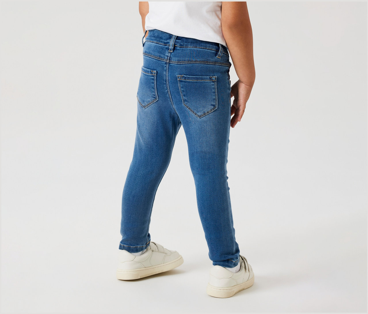 Kind von hinten in NAME IT Kinder-Jeggings und weißen Schuhen.