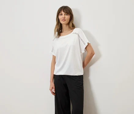 Frau trägt ein weißes T-Shirt mit Lochstickerei an den Ärmeln und eine schwarze Hose.