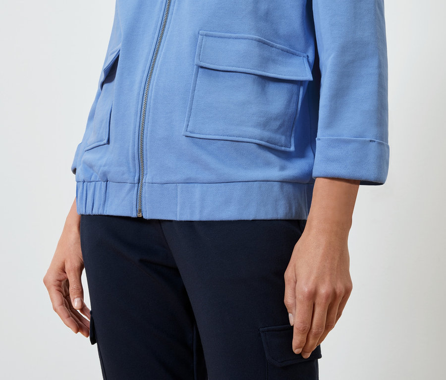 Eine Frau trägt eine hellblaue Jacke und eine dunkelblaue Hose.