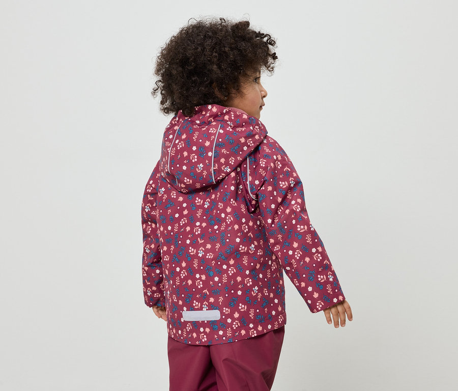Kind mit lockigem Haar, von hinten, trägt eine burgunderfarbene Jacke mit Blumenmuster und eine passende Hose.