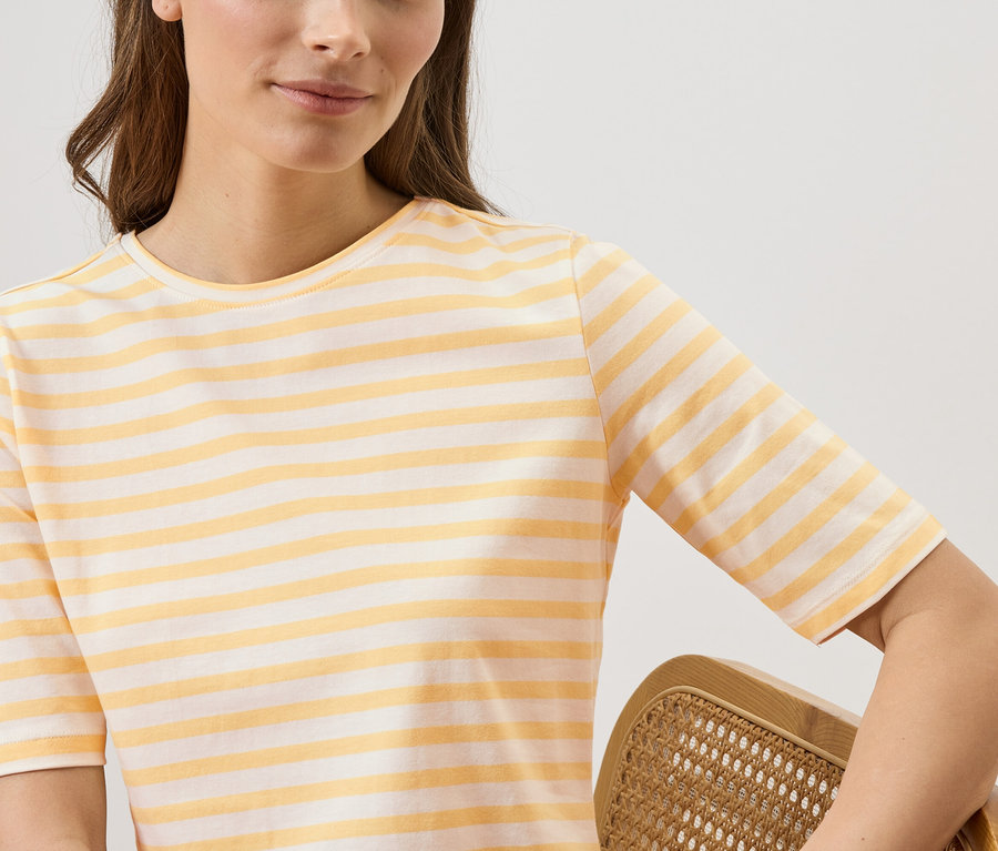 Frau trägt ein gelb-weiß gestreiftes T-Shirt und hält einen Rattanstuhl fest.