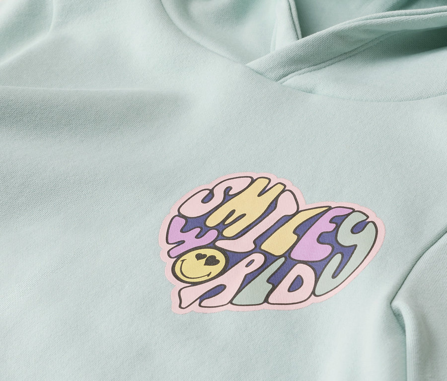 Nahaufnahme eines mintgrünen Hoodies mit einem herzförmigen Smiley-Motiv.