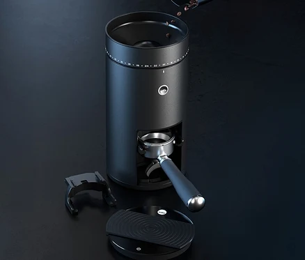 Eine schwarze Kaffeemühle mit Bohnen im Trichter, einem Siebträger und einer Waage auf einem dunklen Tisch.