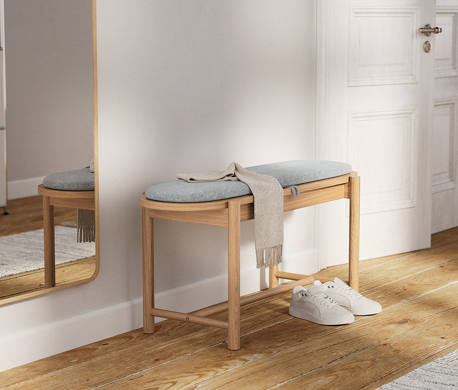 Eine helle Holzbank mit einem hellblauen Kissen und einem beigen Schal liegt darauf. Darunter stehen weiße Turnschuhe.