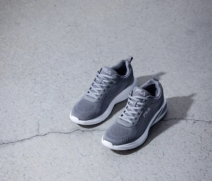 Zwei graue Fila-Sneakers mit weißen Sohlen stehen auf einem grauen Betonboden.