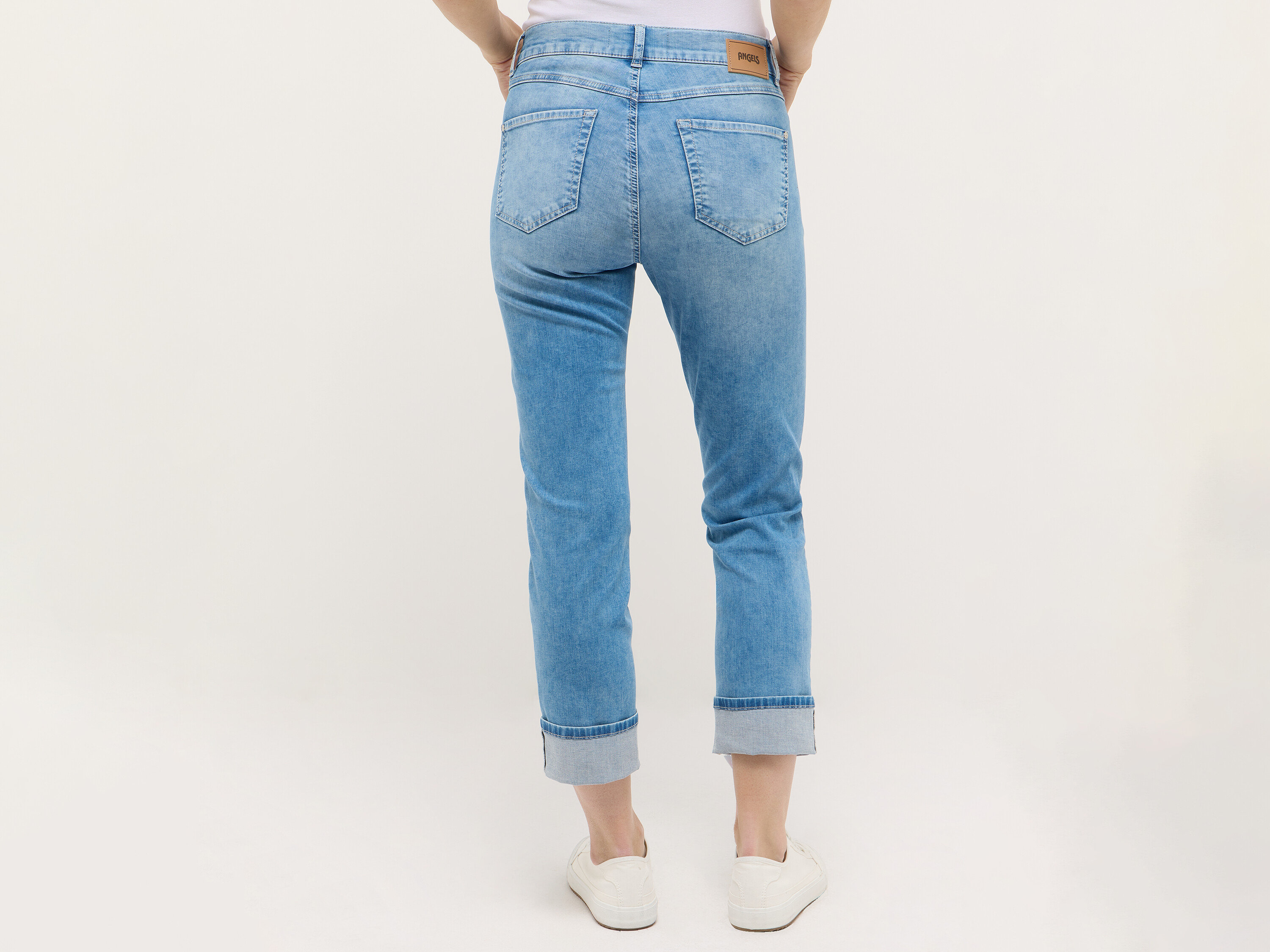 Hüfte und Beine einer Frau in hellblauen Jeans und weißen Sneakers, von hinten aufgenommen.