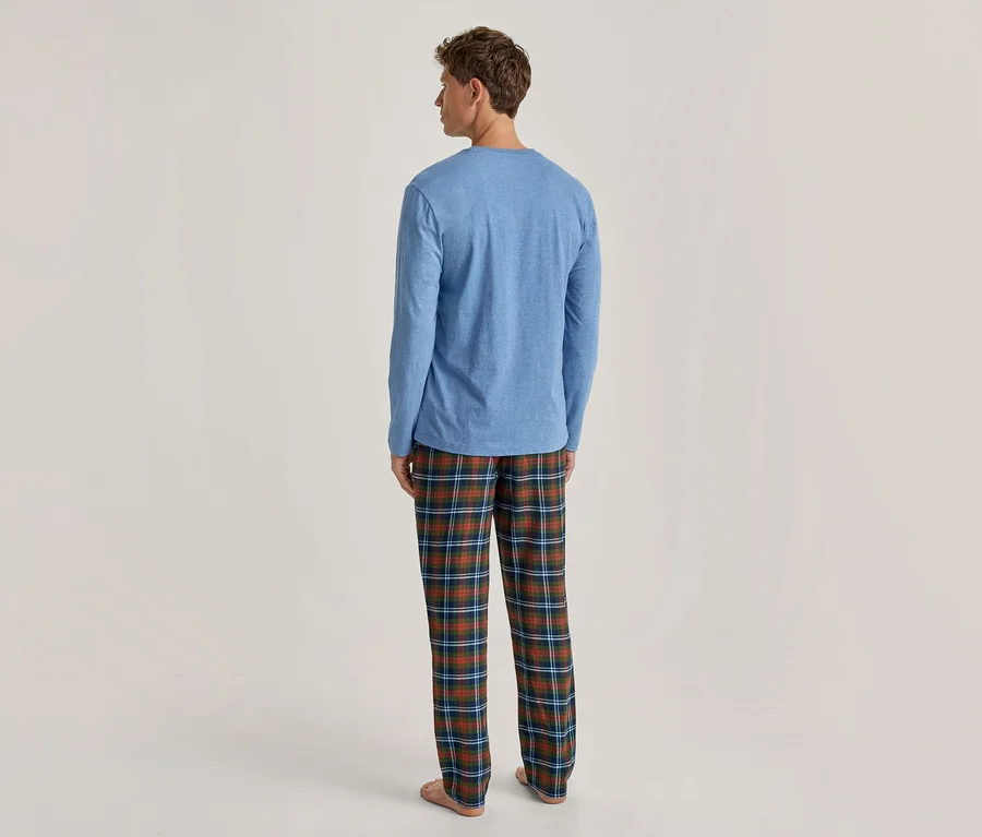 Mann steht mit dem Rücken zum Betrachter, trägt ein blaues Langarmshirt und grün, blau, orange karierte Pyjamahose.
