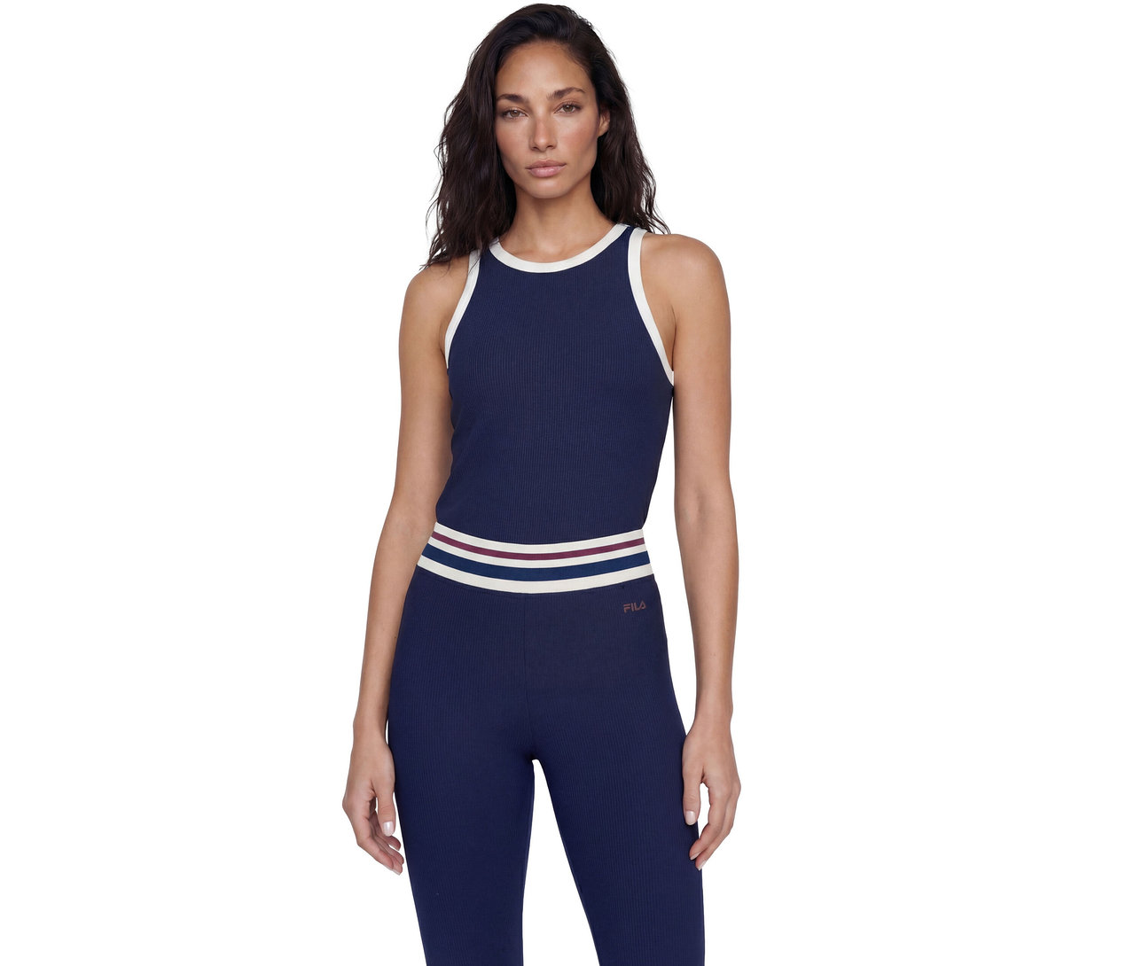 Frau steht in einem marineblauen gerippten Tanktop mit weißem Rand und passenden gerippten Leggings mit gestreiftem Bund und FILA-Logo.