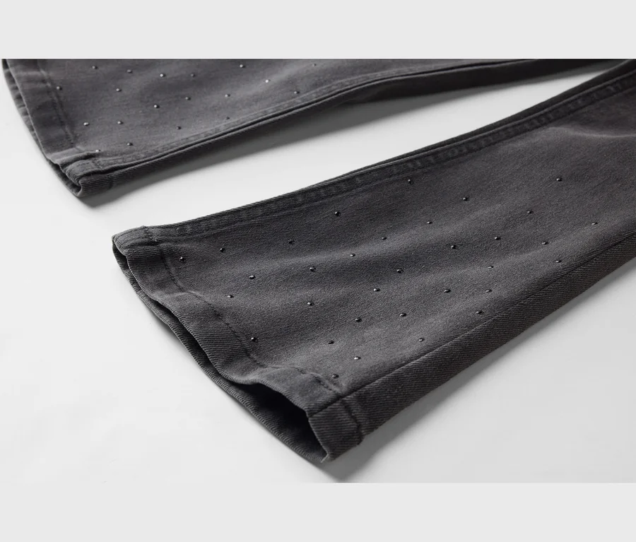 Nahaufnahme von dunkelgrauen Jeans mit kleinen, gleichmäßig verteilten Nieten auf dem Stoff.