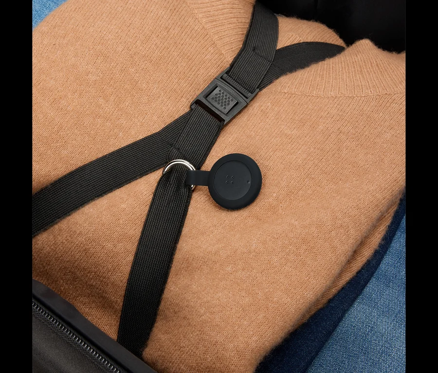Ein brauner Pullover und blaue Jeans liegen in einem Koffer, darüber ein schwarzer Gurt mit einem runden, schwarzen Anhänger.