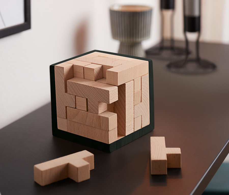 Auf einem Tisch stehen ein IQ-Puzzlewürfel und zwei Teile daneben.