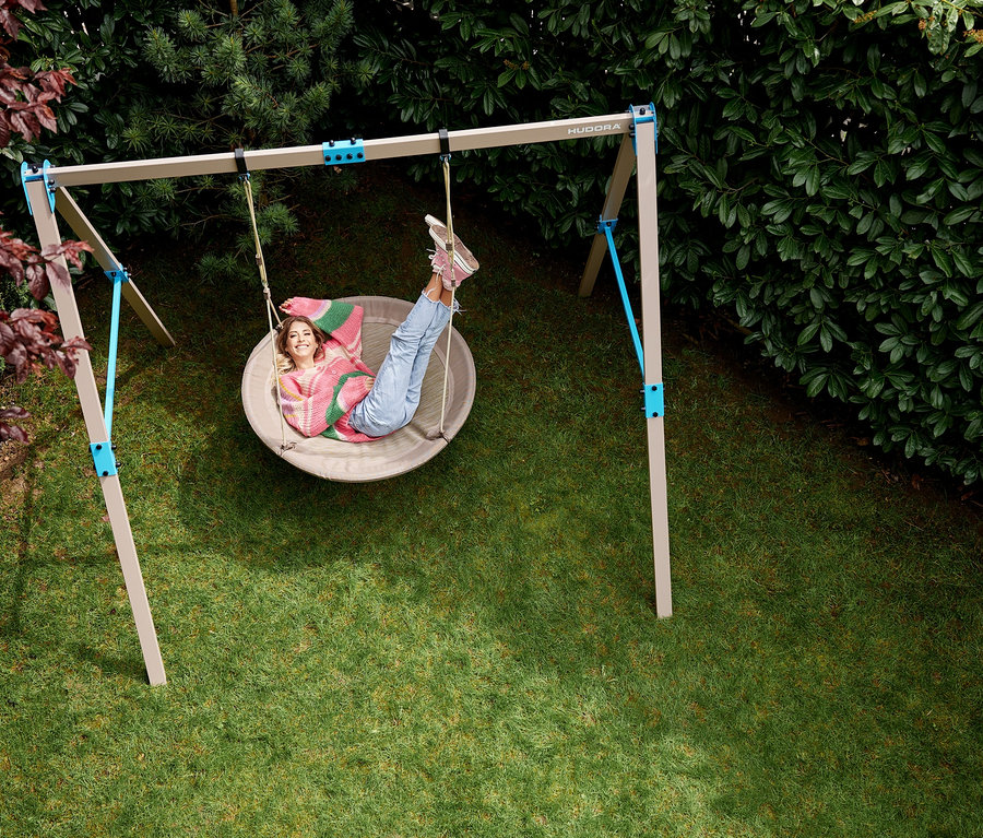 Eine junge Frau liegt in einer beige-farbenen HUDORA Nestschaukel »Lounge« mit einem Durchmesser von 110 cm im Garten.