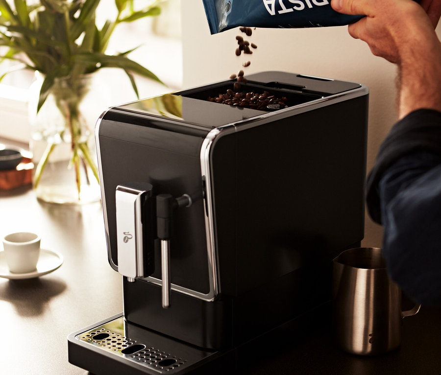 Mann schüttet Kaffeebohnen in den »Esperto Latte« Tchibo Kaffeevollautomaten, Anthrazit.