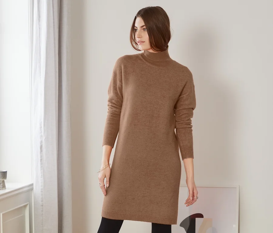 Frau posiert in braunem Strickkleid, schwarzen Leggings und Stiefeln.