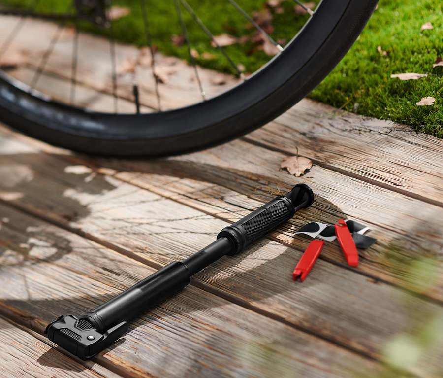Schwarzes Fahrrad steht auf einem Holzboden neben einer Mini-Fahrradpumpe und einem Reperaturset.
