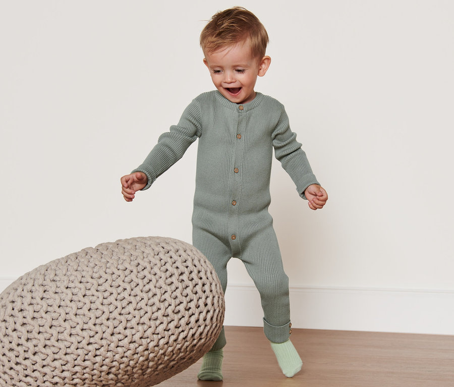 Kleiner Junge im Strickoverall spielt mit einem Strickpouf.