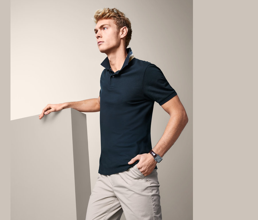 Mann posiert in marineblauem Piqué-Poloshirt und beigen Hosen.