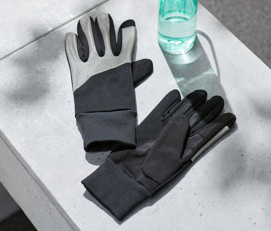 Zwei Windprotection-Handschuhe mit Reflektorbesatz liegen auf einer grauen Oberfläche neben einer Wasserflasche.