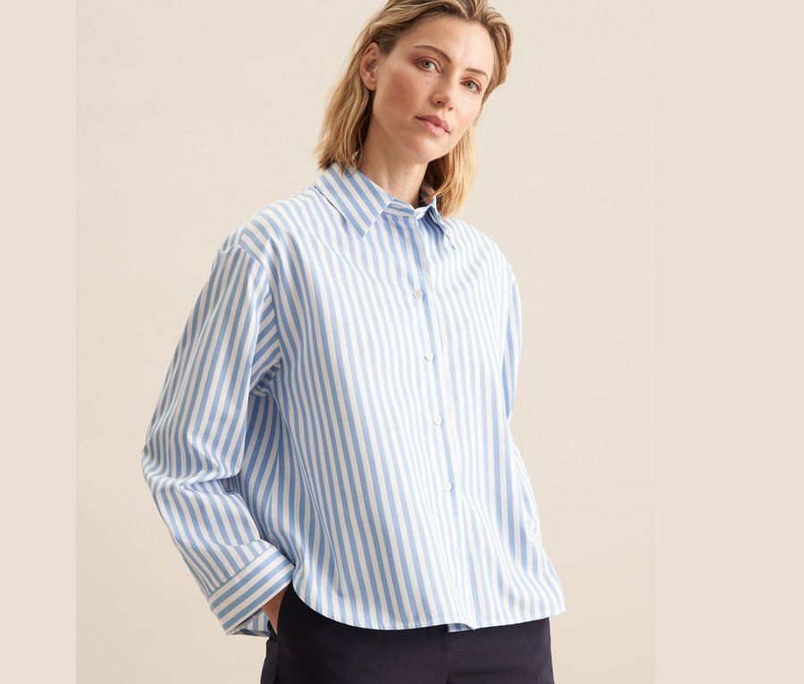Frau trägt eine blaue, gestreifte Seidensticker Oversize Hemdbluse mit weißen Streifen und eine dunkelblaue Hose.