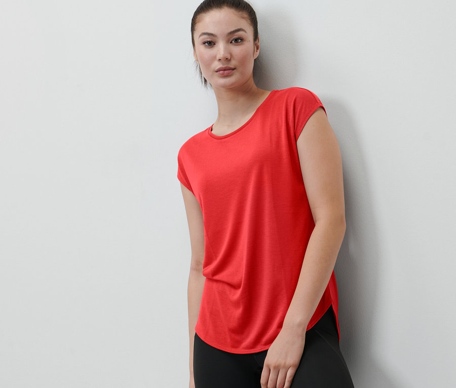 Eine Frau, die sich an eine Wand lehnt, trägt ein rotes Sportshirt.
