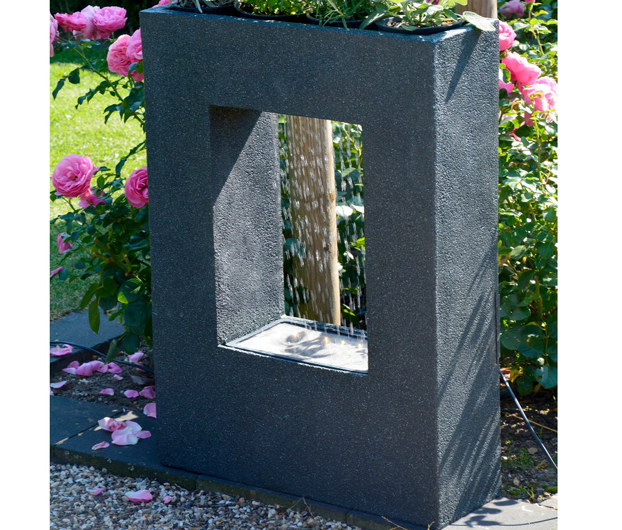 Ein schwarzer Dobar Gartenbrunnen mit Pflanzen-Option steht draußen zwischen Rosen.