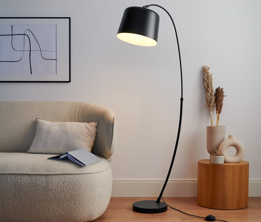 Eine schwarze Bogenleuchte aus Metall steht neben einem beigen Sofa.