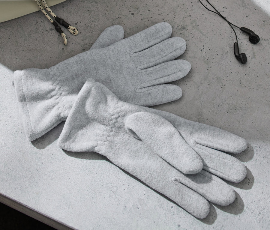 Zwei graue Fleece-Handschuhe liegen auf einer grauen Oberfläche neben Kopfhörern und einer Tasche.