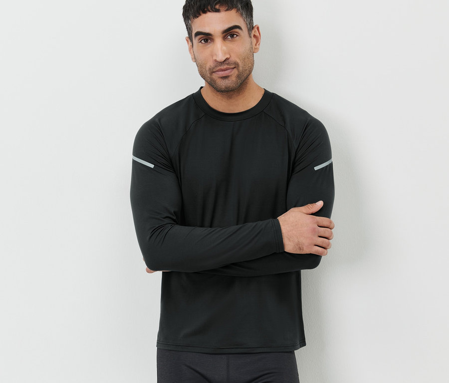 Mann mit verschränkten Armen, der an einer Wand steht und ein schwarzes Langarm-Funktionsshirt trägt.
