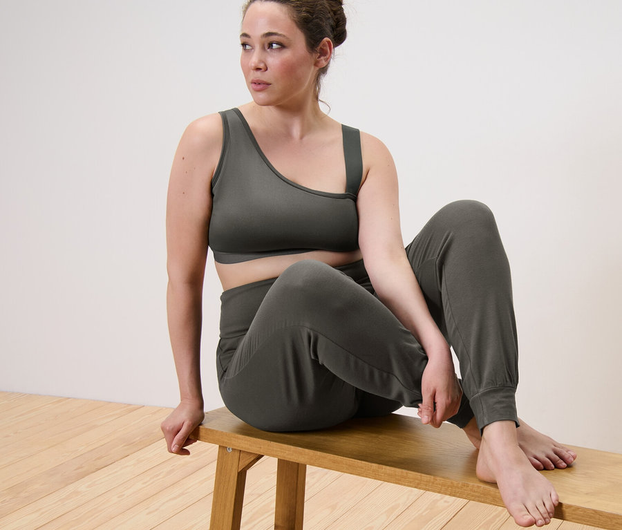 Frau sitzt in Sport-Bustier und Yogahose auf einer Bank.