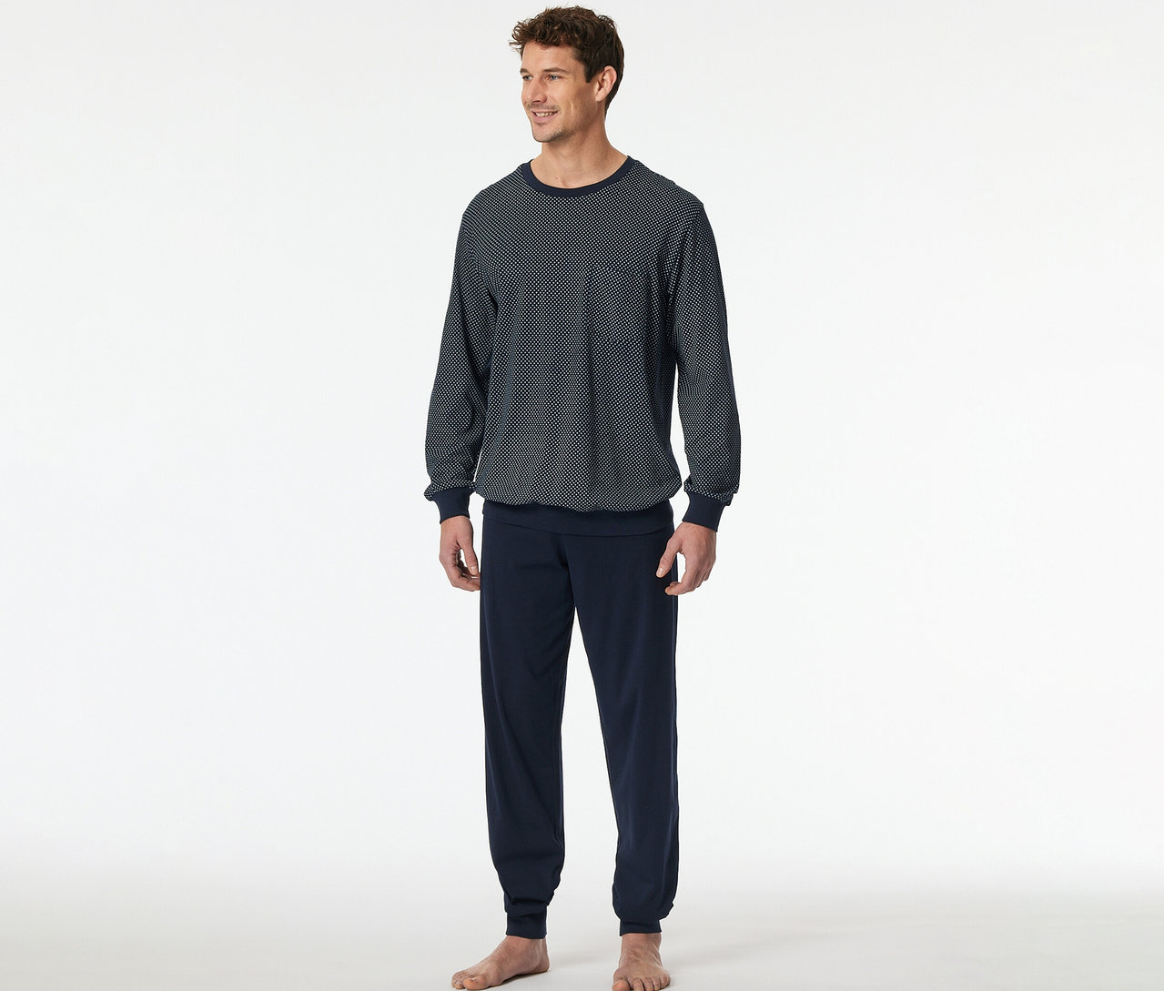 Ein Mann trägt ein SCHIESSER Pyjama-Set. Das Oberteil ist dunkelblau mit weißem Muster und einer Brusttasche, die Hose ist unifarben dunkelblau.